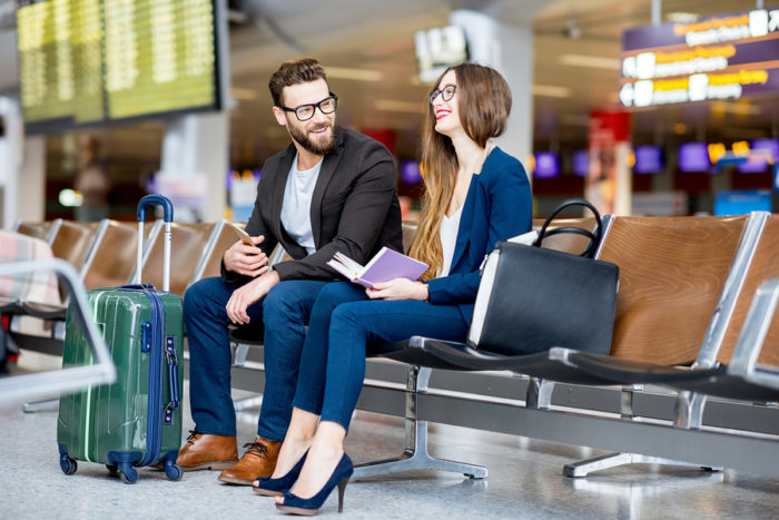 Elegant business couple sitting with phone and book at the waiting hall in the airport. Business travel concept